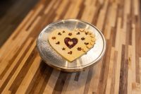 Linzer Tart Hearts Heart-shaped Linzer Tart Hearts cookie with star cutouts showing red jam, dusted with sugar, on metal plate.