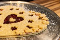 Linzer Tart Hearts Linzer Tart Hearts with a heart-shaped cutout showing red preserve, edged in flower cutouts, dusted with sugar.