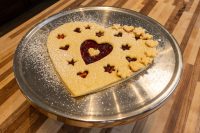 Linzer Tart Hearts Heart-shaped Linzer Tart Hearts with cut-out stars showing red jam, dusted with powdered sugar on a metal plate.