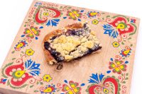 Sheet Kolach with Streusel A slice of Sheet Kolach with Streusel showing dark berry filling and buttery crumb topping on a painted wooden board.