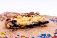 Sheet Kolach with Streusel Cross-section slice of Sheet Kolach with Streusel showing dark berry filling and golden streusel on a wooden board.