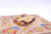 Sheet Kolach with Streusel Slice of Sheet Kolach with Streusel showing streusel topping and dark berry filling on a painted wooden board.