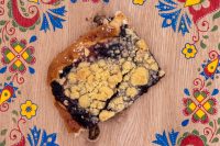 Sheet Kolach with Streusel A broken piece of Sheet Kolach with Streusel showing dark blueberry filling and buttery crumb topping on a wooden board.