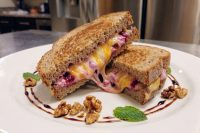 Grilled Cheese with Goat Cheese and Beets halves stacked, oozing melted cheese and purple beets, walnuts and mint on plate