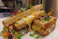 Brie Grilled Cheese Halved Brie Grilled Cheese sandwich oozing melted cheese, topped with microgreens and edible flowers.