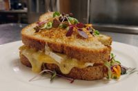 Brie Grilled Cheese Brie Grilled Cheese sandwich with melted cheese oozing from toasted bread, garnished with microgreens on a white plate.