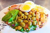 Cobb Salad Cobb Salad on a white plate with avocado, egg, olives, tomato, cheese, ham, and croutons.