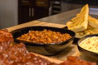 Easy Baked Beans Black dish of Baked Beans in reddish sauce, served with garlic bread, a creamy side, and ribs.