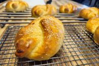 Pletýnka Bun Golden Pletýnka Bun topped with sesame seeds cooling on a wire rack next to smaller buns