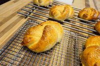Pletýnka Bun Golden braided Pletýnka Buns topped with sesame seeds cooling on wire racks over a wooden counter.