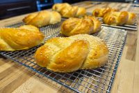 Pletýnka Bun Golden braided Pletýnka Bun rolls, some topped with sesame seeds, cooling on wire racks.