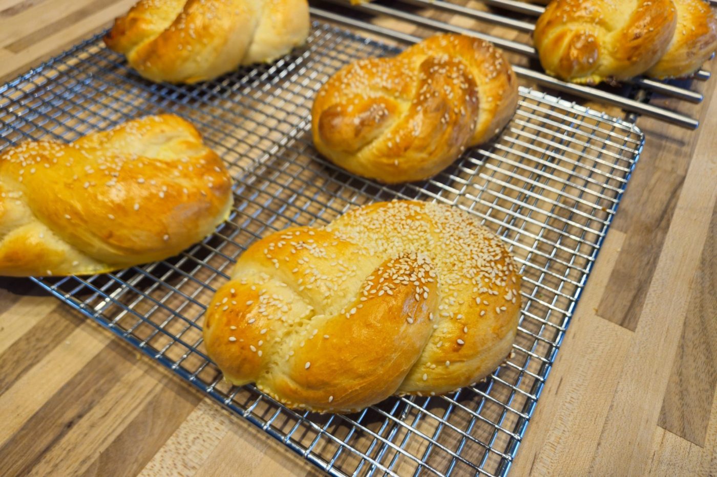 Pletýnka Bun Golden braided Pletýnka Buns with sesame seeds cooling on wire racks over a wooden table.