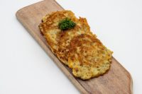 Side Potato Pancakes Bramboráčky Two golden fried Side Potato Pancakes Bramboráčky on a wooden board with a parsley sprig.