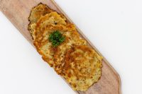 Side Potato Pancakes Bramboráčky Four golden fried Side Potato Pancakes Bramboráčky on a wooden board with curly parsley garnish.