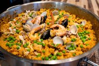 Large metal pan of saffron paella topped with shrimp, mussels, clams, and green peas.
