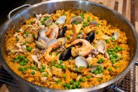 Overhead view of paella pan filled with saffron rice, clams, mussels, shrimp, and peas.