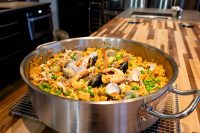 Large steel pan of Paella with saffron rice, clams, mussels, shrimp, and peas.