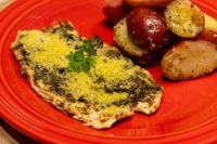 Fish Plated with Baby Potatoes Herb-crusted fish fillet beside Baby Red Potatoes with Butter, peppered and halved, on a red plate.