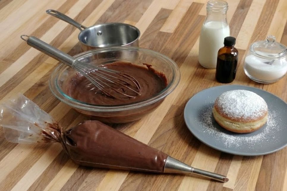 Chocolate Pastry Cream for Filling Pastry in a bowl and piping bag beside a powdered-sugar doughnut and milk.