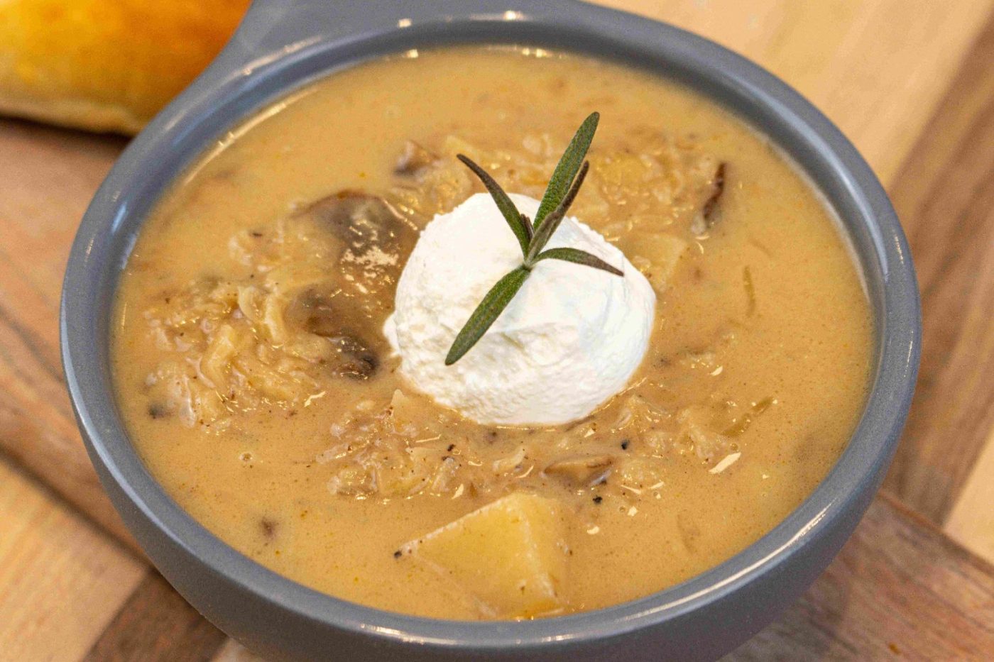 Bowl of Valašská Kyselica Soup topped with a sour cream dollop and a rosemary sprig, with mushrooms and diced potato visible in the broth.